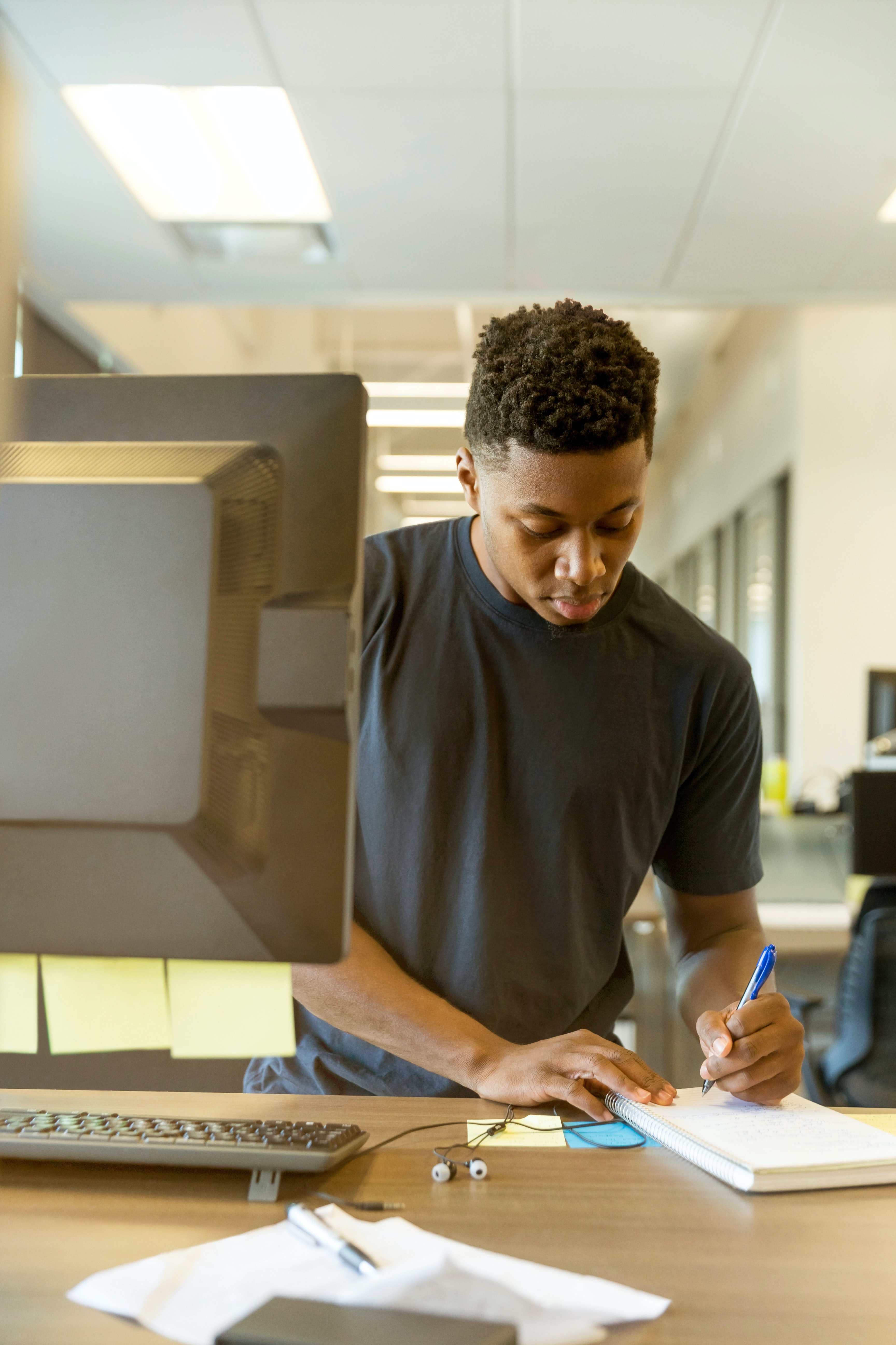 Student writing on a notepad behind his computer